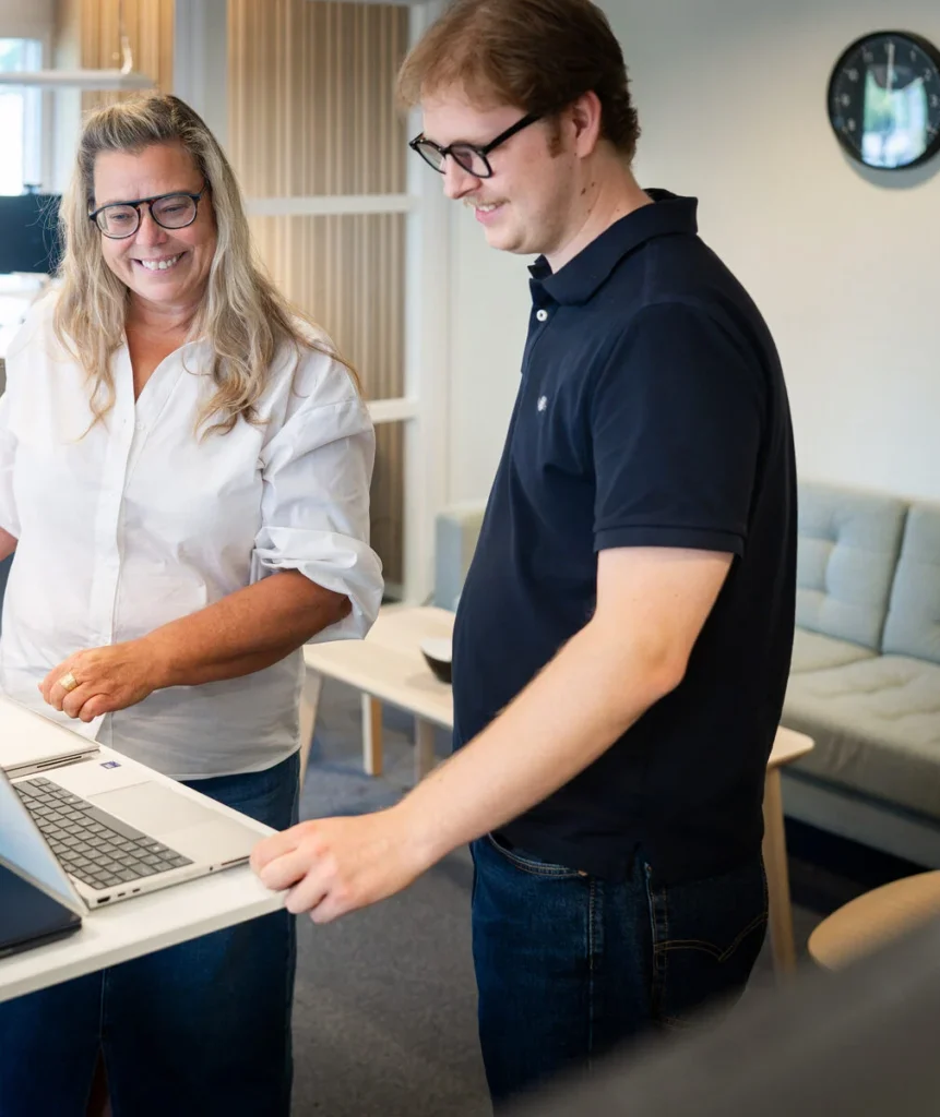 Två medarbetare står vid ett höj- och sänkbart bord med en bärbar dator